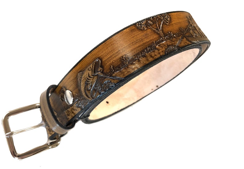 May include: A brown leather belt with a tooled design of a fish jumping out of the water. The belt has a silver buckle.