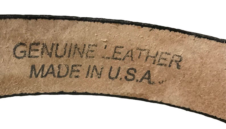 May include: Close-up of a brown leather belt with black stitching. The belt has a label that reads "GENUINE LEATHER MADE IN U.S.A."
