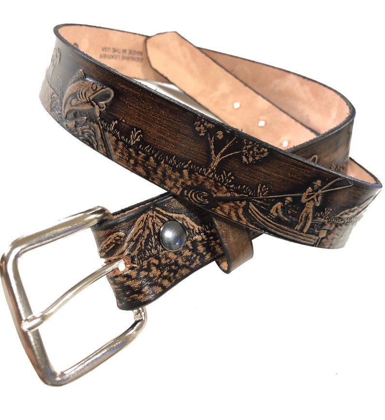 May include: A brown leather belt with a tooled design of a fishing scene. The belt has a silver buckle and is made in the USA.