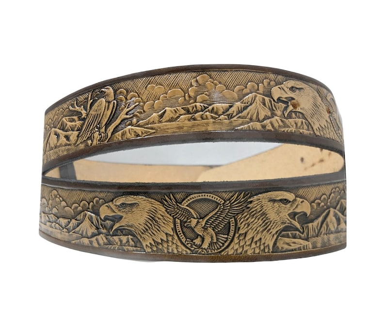 Peut inclure: Une ceinture en cuir marron avec un motif en relief d&eacute;taill&eacute; d'aigles et de montagnes. La ceinture est en cuir de haute qualit&eacute; et pr&eacute;sente un design unique et complexe.
