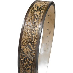 Peut inclure: Une ceinture en cuir marron avec un motif en relief dor&eacute; d'aigles et d'arbres. La ceinture est pr&eacute;sent&eacute;e enroul&eacute;e.