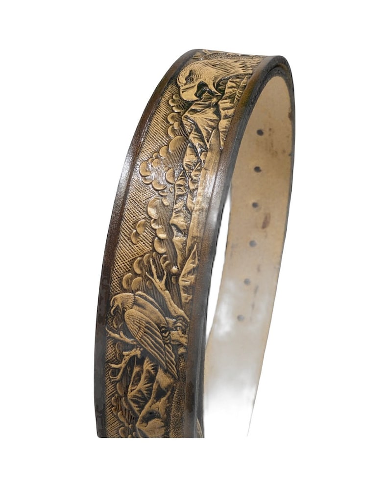 Peut inclure: Une ceinture en cuir marron avec un motif en relief dor&eacute; d'aigles et d'arbres. La ceinture est pr&eacute;sent&eacute;e enroul&eacute;e.