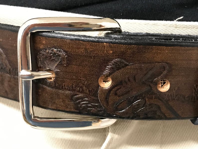 May include: A brown leather belt with a silver buckle. The belt has an embossed design of a fish.