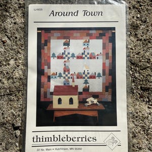 May include: A sewing pattern titled "Around Town" by thimbleberries. The pattern cover features a quilt design with houses and trees. The pattern is in a clear plastic bag.