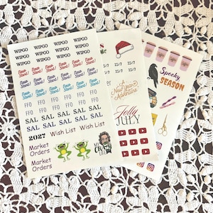 May include: Three sheets of planner stickers with various designs and text. One sheet has text like "WIPGO" and "New Start!", another has a Santa hat and "Jolly July", and the last has "Spooky Season" and coffee cups.