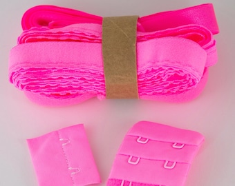 May include: A roll of pink bra strap elastic with a brown paper label. There are two pink bra hook and eye closures.