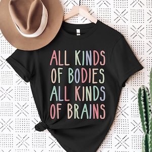Könnte beinhalten: Schwarzes T-Shirt mit dem Text "All Kinds of Bodies All Kinds of Brains" in Regenbogenfarben.
