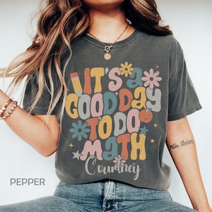 May include: A gray t-shirt with a retro-style graphic that says "It's a good day to do math Courtney". The graphic features colorful letters, flowers, and stars.