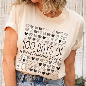 May include: A beige t-shirt with a black graphic design of hearts and the text "100 DAYS OF doing teacher stuff".