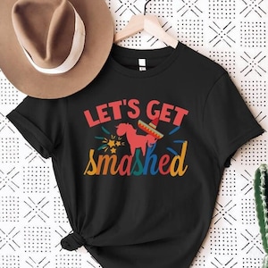 Puede incluir: Camiseta negra con el texto "Let's Get Smashed" en letras de colores con un burro de dibujos animados que lleva un sombrero.