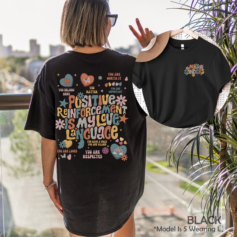 Pode incluir: Camiseta preta com um gr&aacute;fico colorido que diz "Positive Reinforcement Is My Love Language" e inclui frases como "You Are Worth It", "You Matter", "You Are Important", "You Belong Here", "You Are Loved", "You Are Respected", e "You Have A Voice You Are Valued".