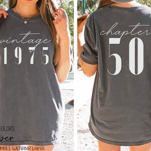 May include: A gray t-shirt with the text "vintage 1975" on the front and "chapter 50" on the back. The shirt is a relaxed fit and has a distressed look.