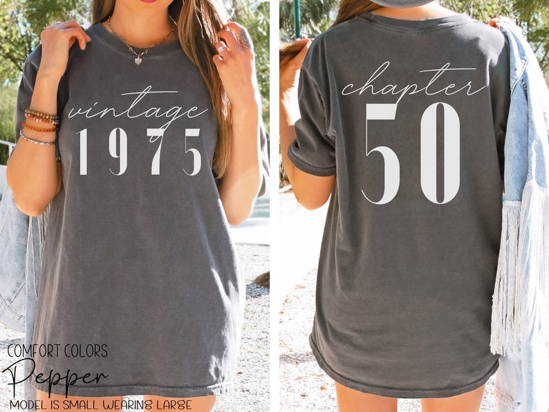 May include: A gray t-shirt with the text "vintage 1975" on the front and "chapter 50" on the back. The shirt is a relaxed fit and has a distressed look.