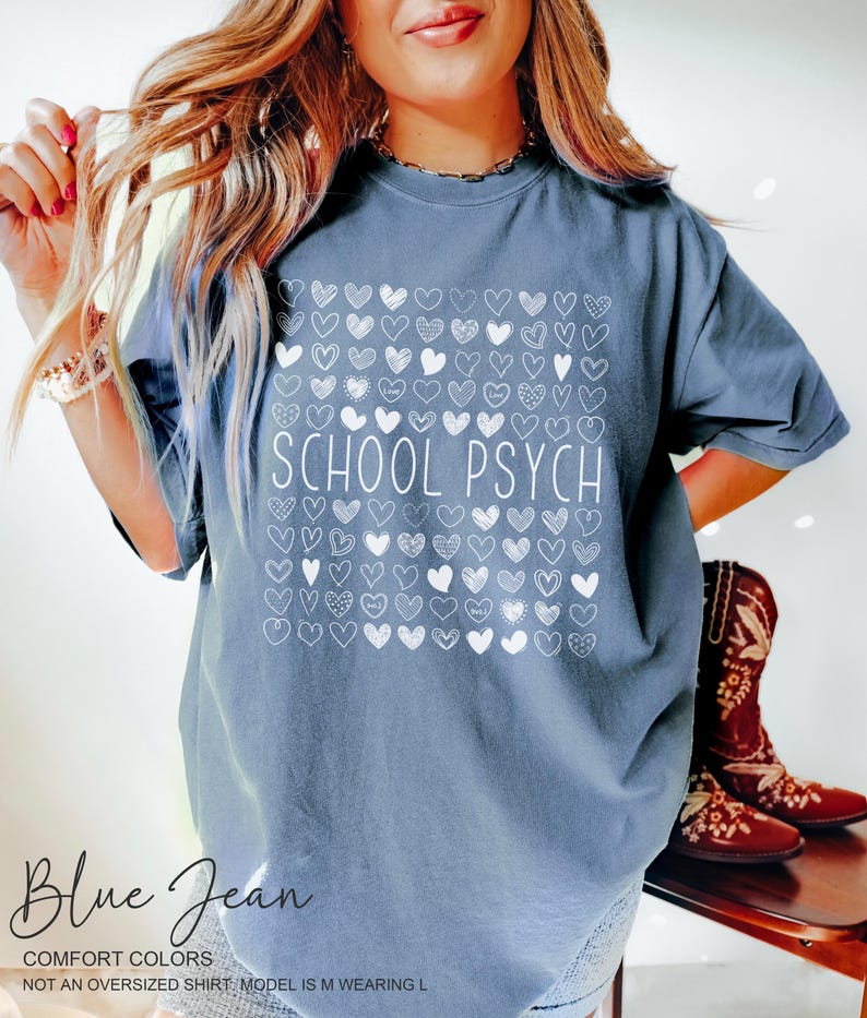 Pode incluir: Camiseta azul jeans com o texto branco "SCHOOL PSYCH", rodeado por um quadrado de cora&ccedil;&otilde;es brancos. A camisa &eacute; de cor confort&aacute;vel e n&atilde;o &eacute; uma camisa grande.