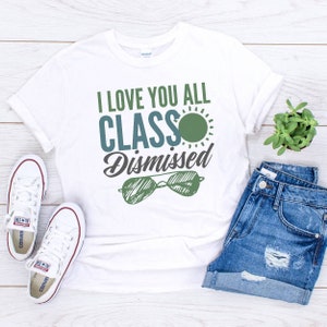 May include: White t-shirt with the text "I love you all class dismissed" in blue and green lettering. A green sun with a blue outline is above the word "class". A pair of sunglasses with a green frame and blue lenses are below the text.