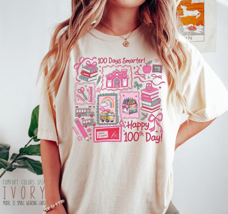 May include: Ivory-colored t-shirt with a colorful graphic celebrating the 100th day of school. The design includes school buses, books, pencils, and the text "100 Days Smarter!" and "Happy 100th Day!" in pink.