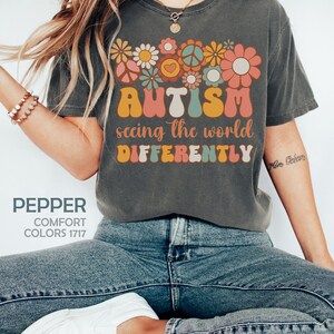 May include: A gray t-shirt with a colorful graphic design featuring flowers, peace signs, and the text "AUTISM seeing the world DIFFERENTLY".