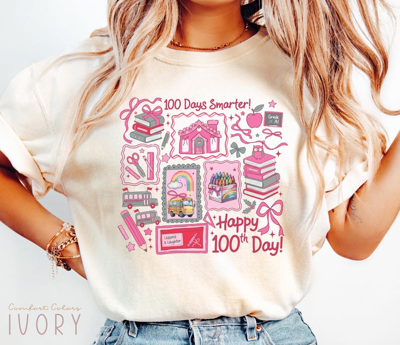 May include: Ivory-colored t-shirt with a colorful graphic celebrating the 100th day of school. The design includes school-themed illustrations such as books, pencils, a school bus, and the text "100 Days Smarter!" and "Happy 100th Day!"