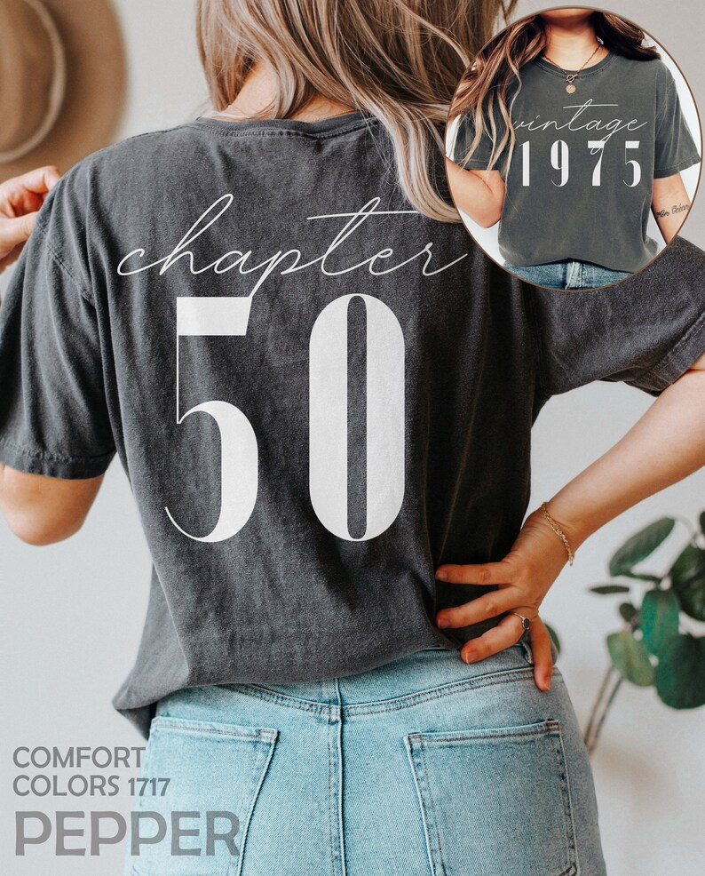 May include: A dark gray t-shirt with the text "chapter 50" printed on the back in white. The front of the shirt has the text "vintage 1975" printed in white.