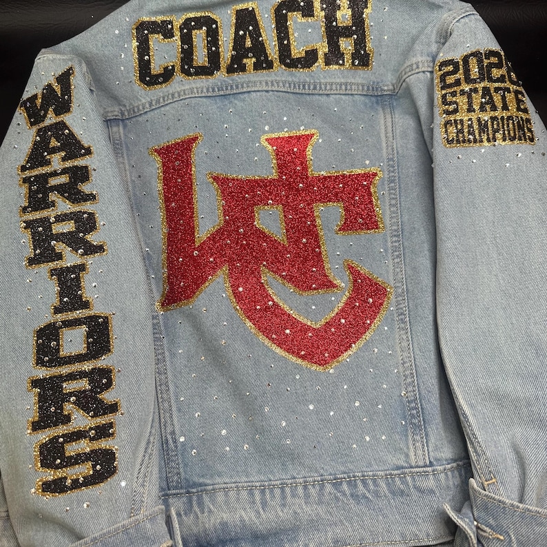 May include: A light blue denim jacket featuring the word COACH in black and gold glitter, the word WARRIORS in black and gold on the sleeve, and 2024 STATE CHAMPIONS on the other sleeve. A large red and gold glitter logo sits in the center.