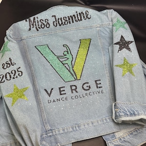 May include: A light blue denim jacket featuring the text Miss Jasmine, est. 2025, and Verge Dance Collective. The back displays a large green glitter V logo with a dancer silhouette, accented by scattered rhinestones and green and black stars.