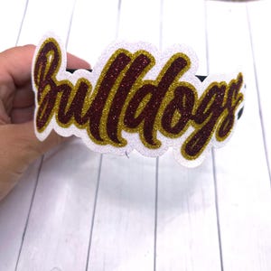 May include: White headband with the word "Bulldogs" in red and gold glitter lettering.