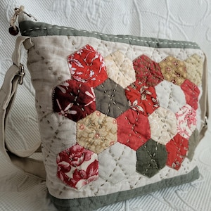 Peut inclure: Sac bandoulière matelassé avec un motif patchwork hexagonal. Le sac présente des tissus floraux et à motifs rouges, crème et bruns. Il a un corps en lin de couleur neutre, une bordure verte et une longue bandoulière réglable.