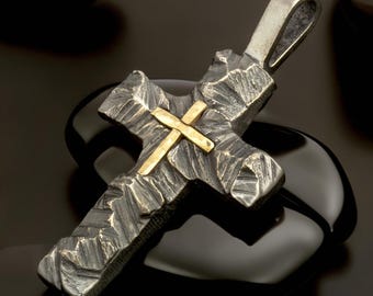 May include: A cross pendant featuring a dark, oxidized silver base with a heavily textured, rugged surface. A smaller, smooth, polished gold-toned cross is layered over the center of the larger silver cross, which includes a sturdy top bail.