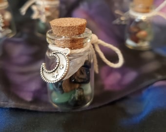 May include: A small glass jar filled with various crystals and topped with a cork stopper. A silver crescent moon charm hangs from the jar.