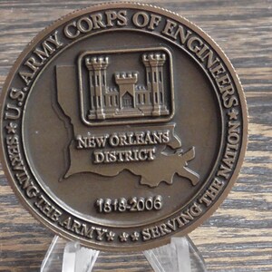 May include: A bronze-colored commemorative coin for the U.S. Army Corps of Engineers, New Orleans District. The coin features a detailed depiction of a fortress and the Louisiana outline, with text including "Serving the Army" and "1818-2006."