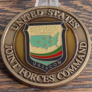 May include: A gold-colored coin with the words "United States Joint Forces Command" and "USJFCOM" on it. The coin features a shield with a map of the United States and five stars.