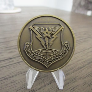 Puede incluir: Una moneda de color bronce con un diseño de estrella y rayo. El texto "Tanker Airlift Control Center" está inscrito alrededor del borde.