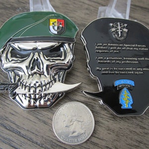 Puede incluir: Una calavera de plata con un gorro verde con un parche amarillo y negro, sosteniendo un cuchillo de plata entre los dientes. La parte posterior de la moneda presenta una silueta negra de un soldado con un parche azul y amarillo y un texto que dice: "¡Soy un soldado de las Fuerzas Especiales de Estados Unidos! Haré todo lo que mi nación me exija. Soy un voluntario, consciente de los peligros de mi profesión. Mi objetivo es tener éxito en cualquier misión y vivir para tener éxito de nuevo. Fuerzas Especiales Aerotransportadas."