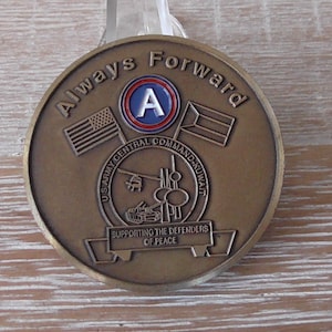May include: A bronze-colored coin with the words "Always Forward" and the US Army Central Command-Kuwait emblem. The coin features the American and Kuwaiti flags, and the text "Supporting the Defenders of Peace".