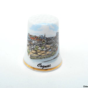 May include: White porcelain thimble with a gold trim and a colorful illustration of a cityscape with the word "Cognac" printed on the bottom.