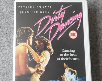 May include: A VHS tape of the movie "Dirty Dancing" featuring Patrick Swayze and Jennifer Grey. The title is in pink script, with the tagline "Dancing to the beat of their hearts."