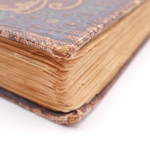 K&ouml;nnte beinhalten: Nahaufnahme des Buchr&uuml;ckens eines alten, abgenutzten Buches mit braunem Lederbezug und goldenen Verzierungen. Die Seiten sind vergilbt und die Kanten sind ausgefranst.