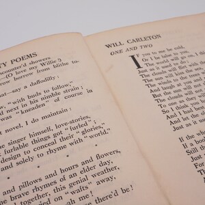 K&ouml;nnte beinhalten: Ein Vintage-Buch mit cremefarbenem Einband und schwarzem Text. Der Titel des Buches lautet "Dainty Poems" und der Autor ist "Will Carleton". Das Buch ist auf einer Seite mit einem Gedicht mit dem Titel "One and Two" aufgeschlagen.