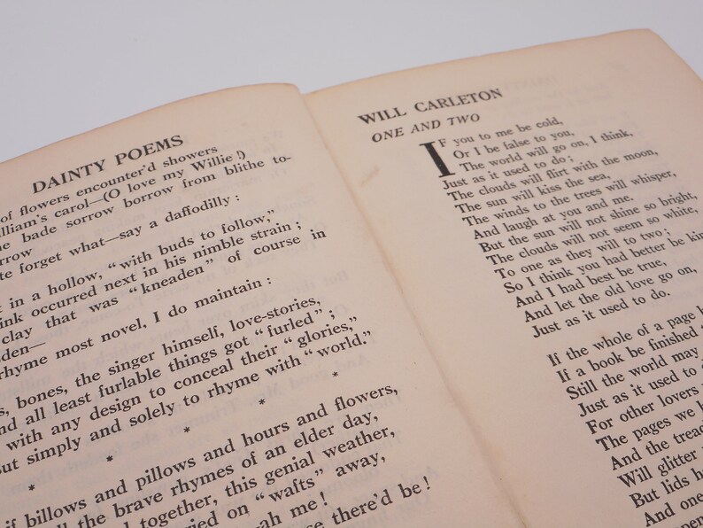 K&ouml;nnte beinhalten: Ein Vintage-Buch mit cremefarbenem Einband und schwarzem Text. Der Titel des Buches lautet "Dainty Poems" und der Autor ist "Will Carleton". Das Buch ist auf einer Seite mit einem Gedicht mit dem Titel "One and Two" aufgeschlagen.