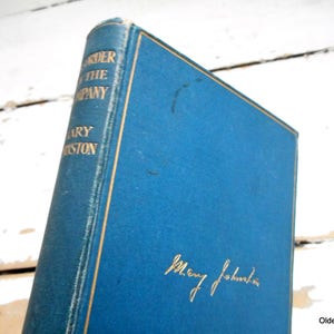 Könnte beinhalten: Ein blaues Hardcover-Buch mit goldenen Lettern auf dem Rücken. Der Titel lautet "Under the Company" von Mary Johnston. Das Buch ist auf dem Einband mit "Mary Johnston" in goldener Tinte signiert.