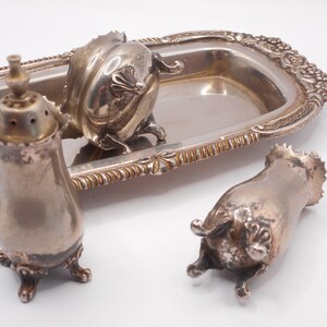 May include: A silver serving tray with ornate detailing, holding three silver salt and pepper shakers with intricate designs.