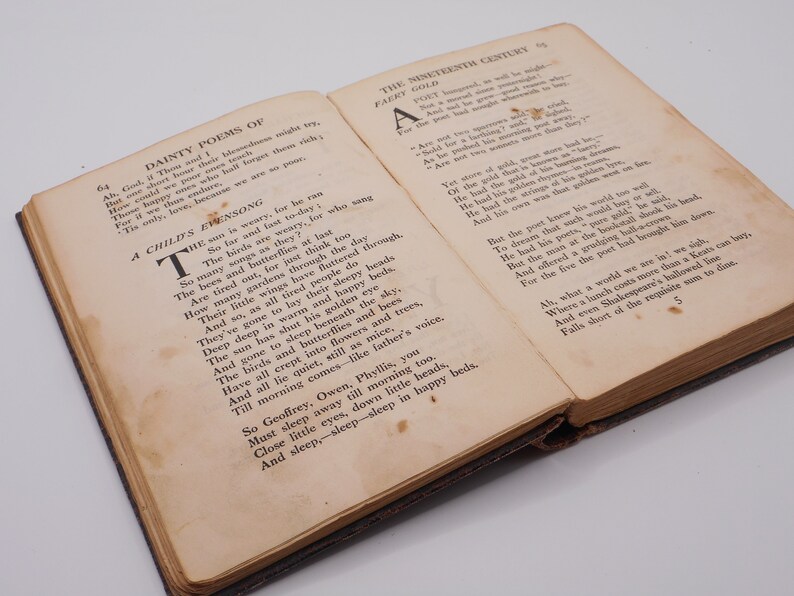 K&ouml;nnte beinhalten: Ein offenes Buch mit vergilbten Seiten, das ein Gedicht mit dem Titel "A Child's Evensong" und ein weiteres Gedicht mit dem Titel "Faery Gold" zeigt. Das Buch ist in braunes Leder gebunden und hat einen abgenutzten, antiken Look.