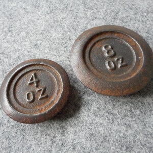 Puede incluir: Dos pesas de hierro fundido oxidadas, una marcada con "4 oz" y la otra con "8 oz".