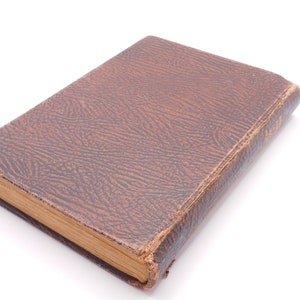 K&ouml;nnte beinhalten: Ein braunes, ledergebundenes Buch mit einem strukturierten Einband. Das Buch ist geschlossen und liegt flach auf einer wei&szlig;en Oberfl&auml;che.