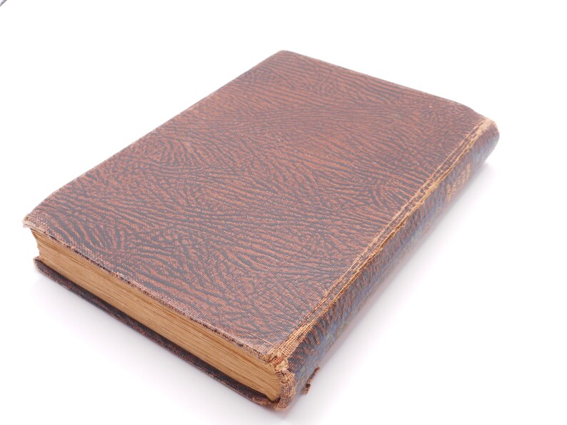 K&ouml;nnte beinhalten: Ein braunes, ledergebundenes Buch mit einem strukturierten Einband. Das Buch ist geschlossen und liegt flach auf einer wei&szlig;en Oberfl&auml;che.