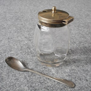 May include: A clear glass jar with a silver lid and a small silver spoon. The jar has a faceted design and the lid has a small handle.