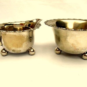 May include: A silver creamer and sugar bowl set with a decorative scalloped edge and three ball feet.