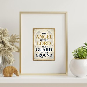 Könnte beinhalten: Gerahmtes rechteckiges Schild mit dem Text "THE ANGEL OF THE LORD IS A GUARD ON THIS GROUND". Das Schild hat einen goldenen Rand und zeigt Engelsflügel. Der Rahmen ist goldfarben und der Hintergrund ist weiß.