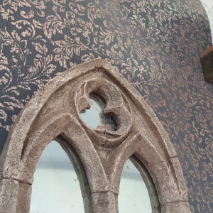 May include: A decorative mirror with a stone-like finish and an arched frame. The mirror has two arched windows with a smaller arched window at the top.