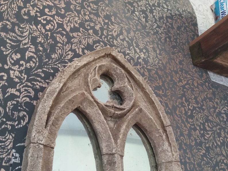May include: A decorative mirror with a stone-like finish and an arched frame. The mirror has two arched windows with a smaller arched window at the top.